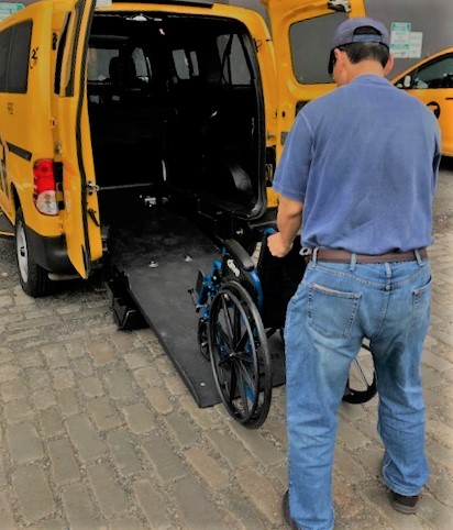A taxi driver is at a training course. He is learning how to secure a wheelchair into his wheelchair accessible taxi.